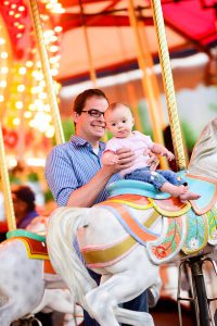 A father holding his baby up on a carousel.