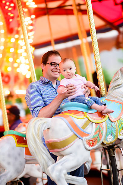 A father holding his baby up on a carousel.